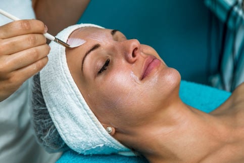 A professional using a fan brush to apply a medical-grade chemical peel solution to a client's forehead